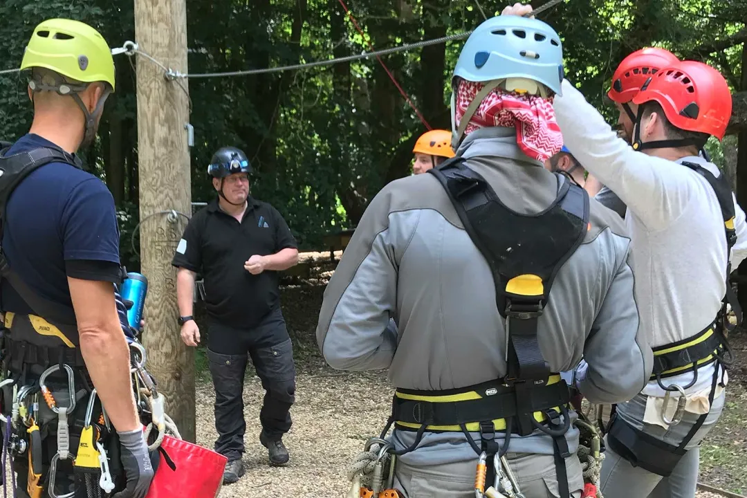 A group of ropes course staff in helmets and harnesses getting ready before a session