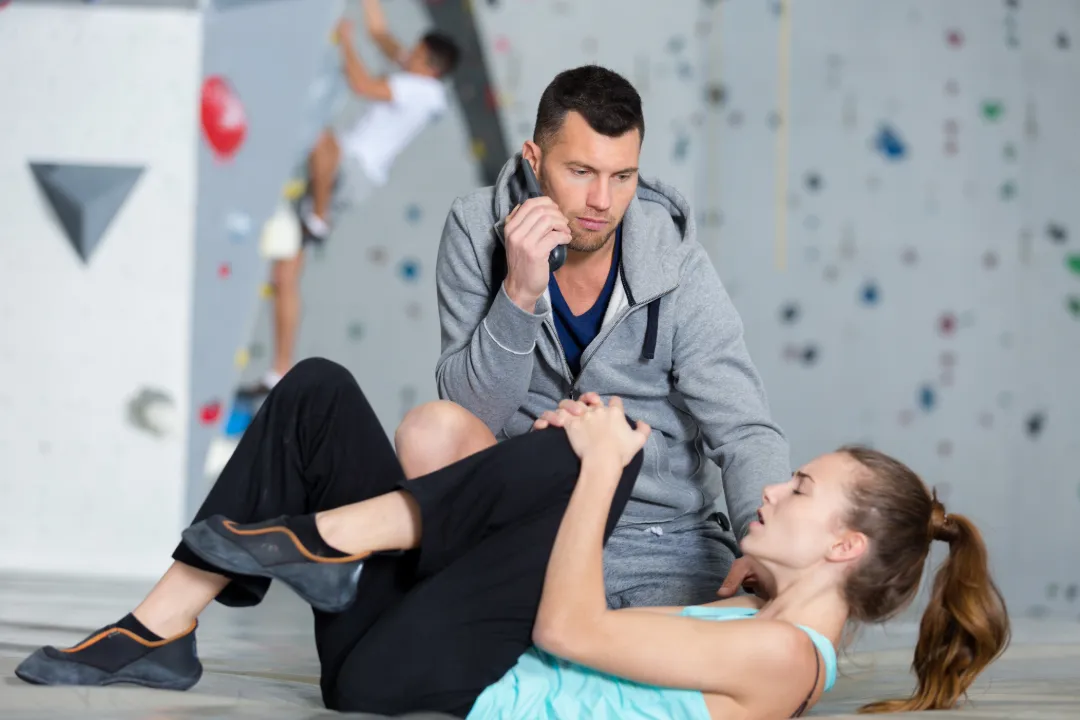 A climbing instructor on the phone tending to an injured climber on a bouldering wall mat
