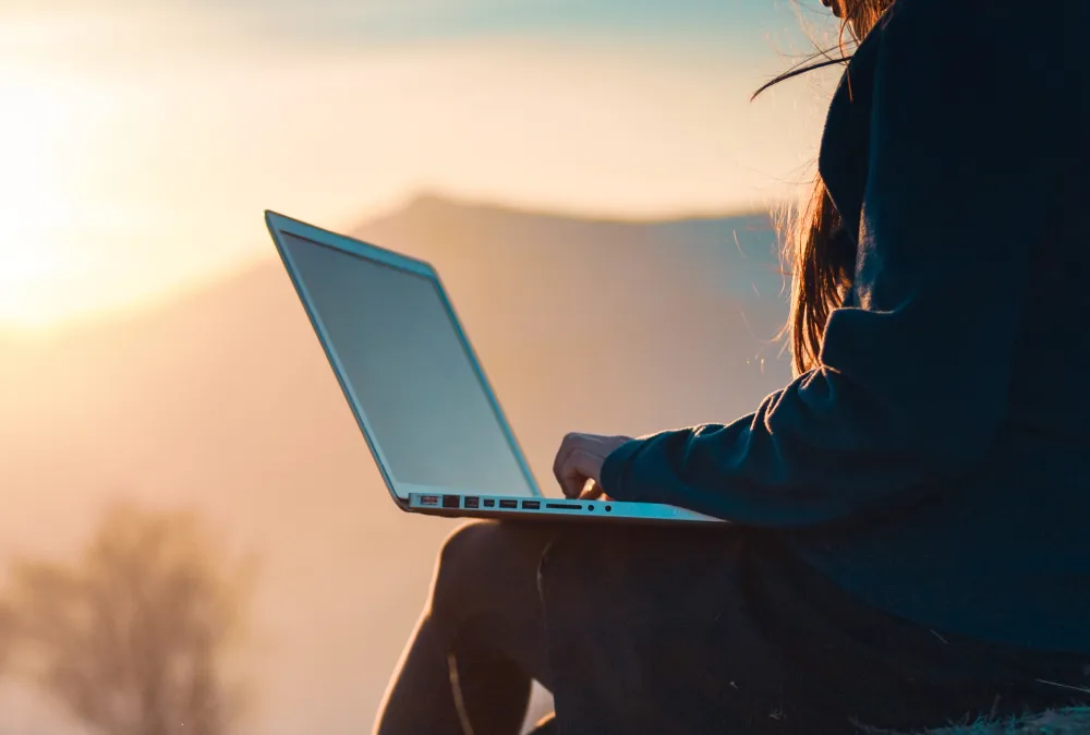 Someone working on a laptop outdoors at sunset with hills in the background