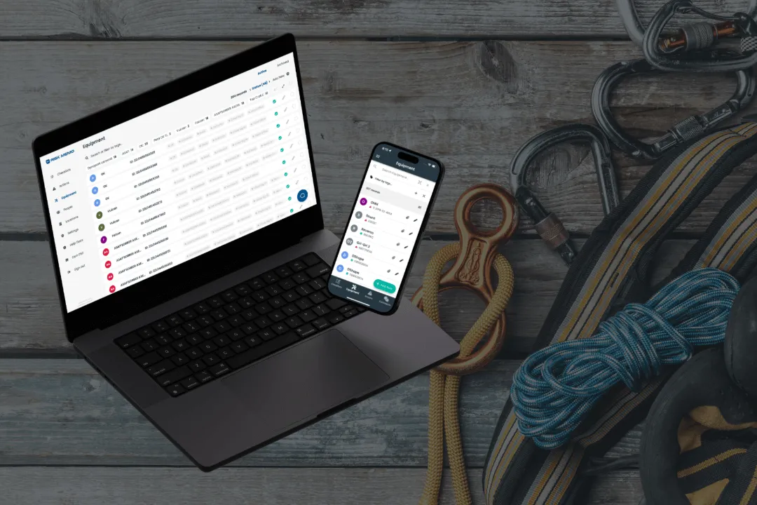 A laptop and phone showing the Risk Memo equipment list next to a coiled climbing rope and carabiners